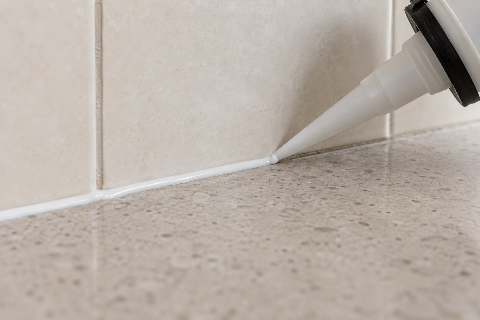 AI-generated close-up of a nozzle applying white silicone where a tiled splashback meets a stone benchtop